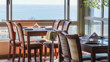 A dining area with a table and chairs, a view of the ocean, and a window with a plant.