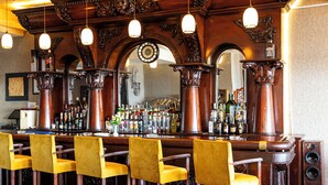 Eine Bar mit Holzausstattung, zahlreichen Flaschen Alkohol und gelben Stühlen.