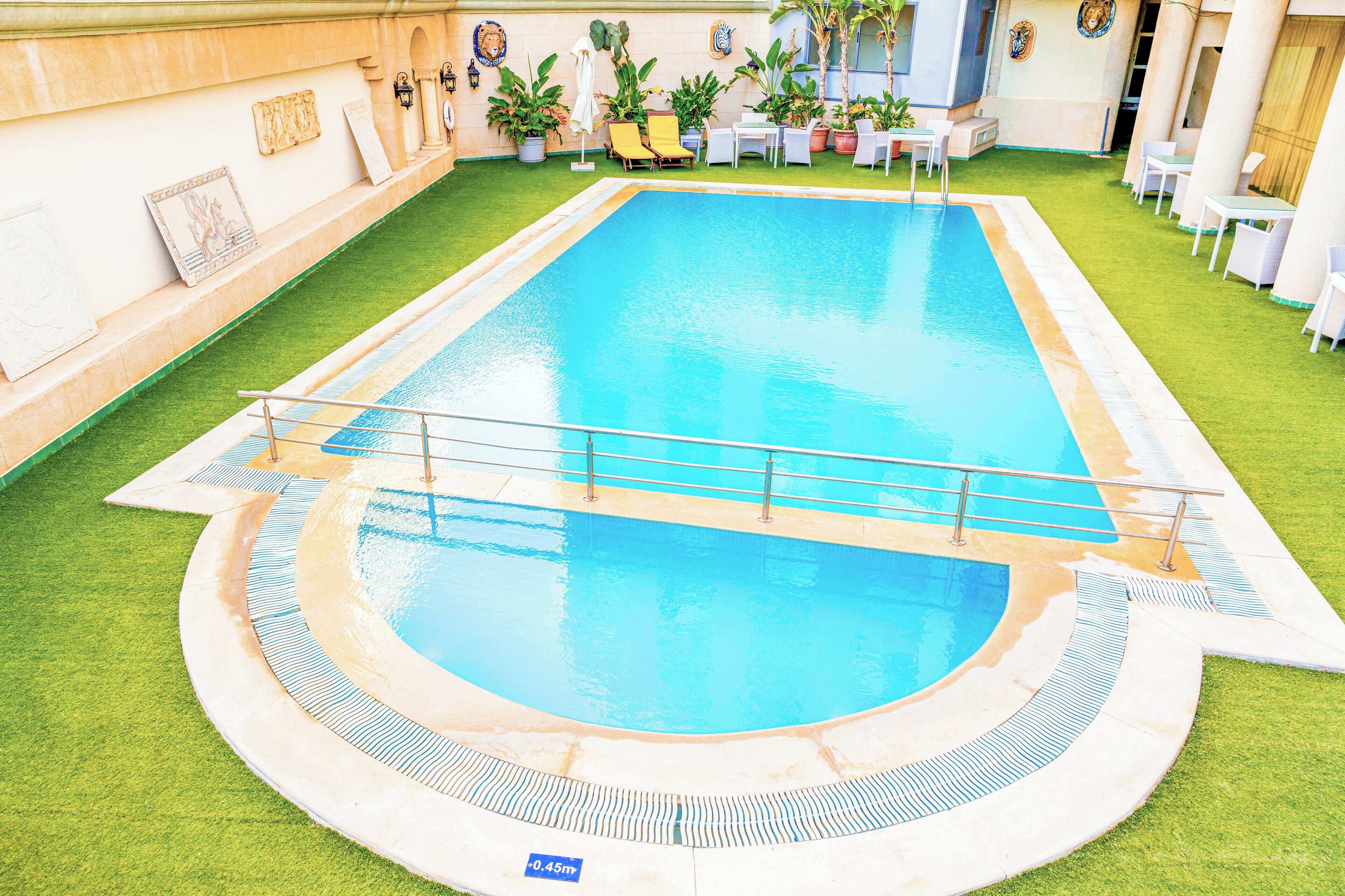 Ein rechteckiger Pool mit einer umlaufenden Holzterrasse, einer kleinen Brücke und einigen Liegestühlen.