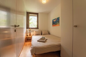 Une chambre à coucher avec un lit, une table de chevet, une fenêtre et un tableau accroché au mur.