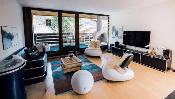 A modern living room with a large TV, comfortable seating, and a view of the outdoors.