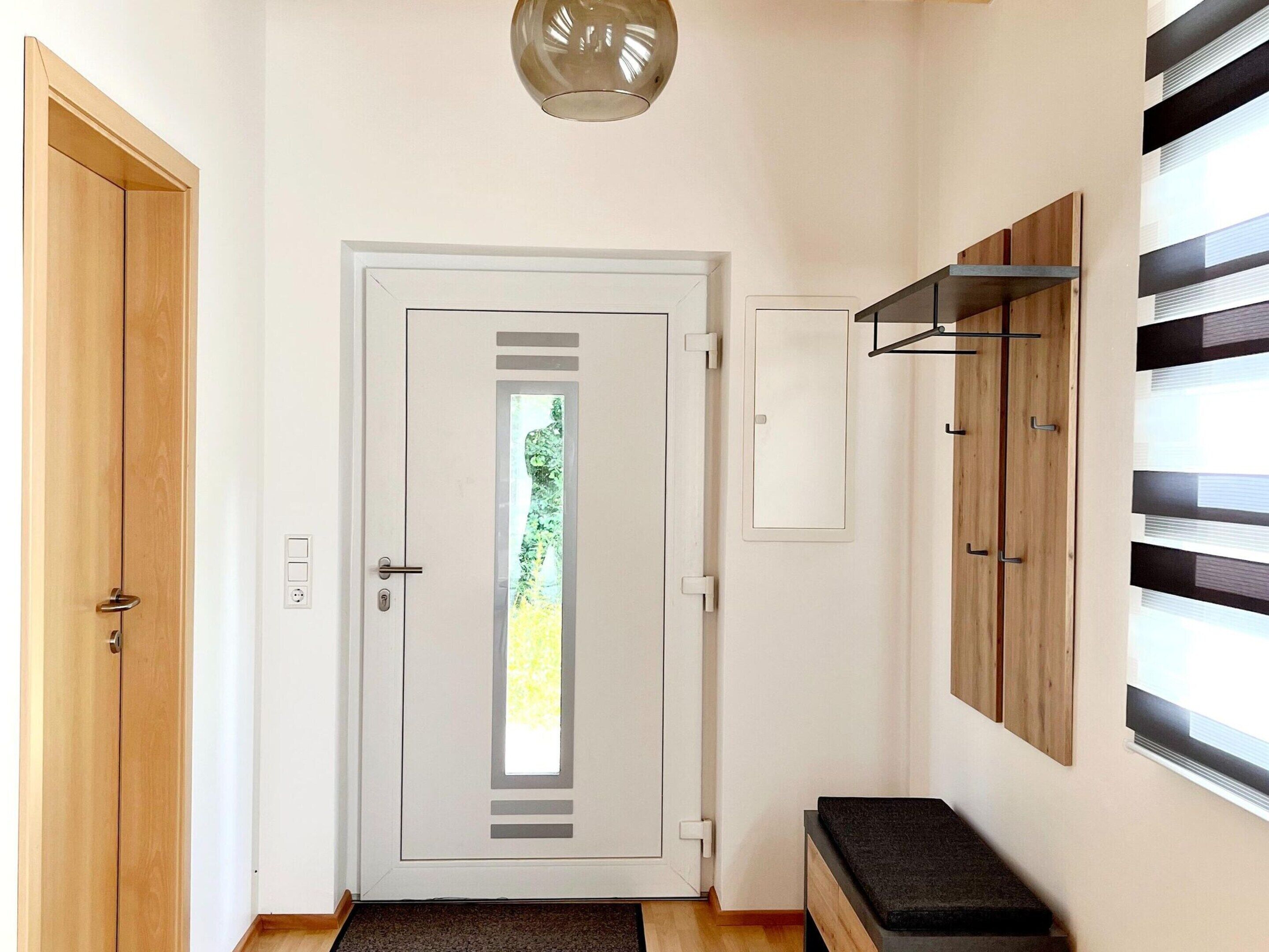 Un couloir avec une porte blanche, un banc et une étagère fixée au mur.