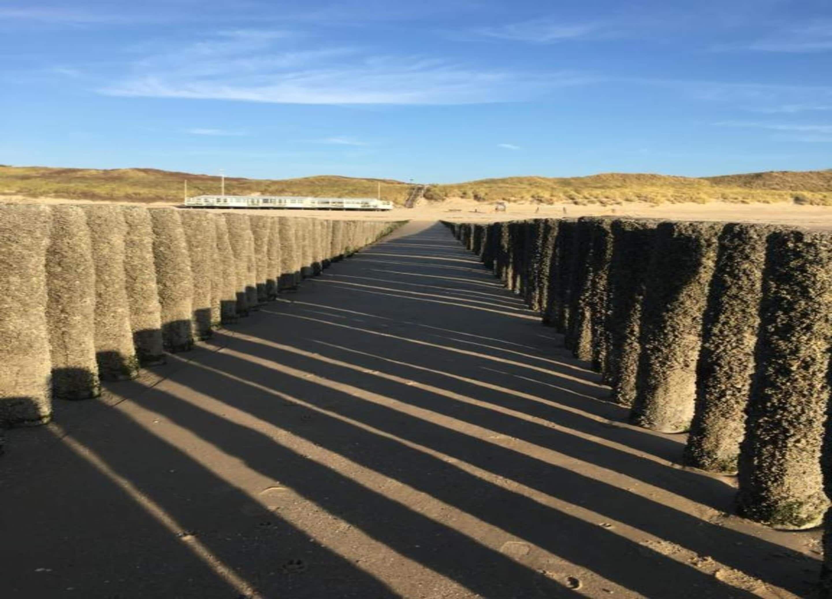 A long, straight pathway with evenly spaced concrete pillars, leading to a distant structure.