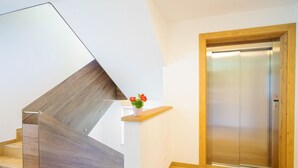 Una moderna scala con finitura in legno, un piccolo ripiano con una pianta in vaso e una porta dell'ascensore con cornice in legno.