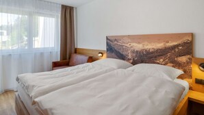 Una camera d'albergo con un letto, una sedia, un quadro appeso e una finestra con tende.