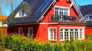 A red house with a balcony, a sloped roof, and a window with a white frame. - Holiday Apartment Luttje Bangbux (Zingst)