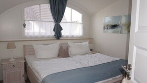 A bedroom with a bed, a nightstand, a window with curtains, and a door. - Holiday Apartment Luttje Bangbux (Zingst)