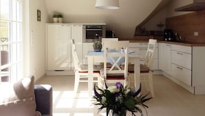 A modern kitchen with white cabinets, a dining table with chairs, and a hanging light fixture. - Holiday Apartment Luttje Bangbux (Zingst)