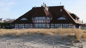 A traditional half-timbered house with a steeply pitched roof, large windows, and a sandy foreground. - Holiday Apartment Luttje Bangbux (Zingst)