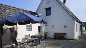 A patio area with a table and chairs under a blue umbrella, a wooden bench, and a white building with a sloped roof. - Holiday Home Alte Liebe Busum (Büsum)