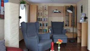 A living room with two grey armchairs, a bookshelf, a small table with a bottle and flowers, and a red bottle on the floor. - Holiday Home Alte Liebe Busum (Büsum)