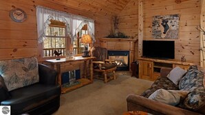 A cozy cabin interior with a fireplace, wooden walls, a television, and a dining area. - Private Wooded Log Cabin Near Shanty Creek Resorts -Four Season Adventure Awaits (Bellaire)