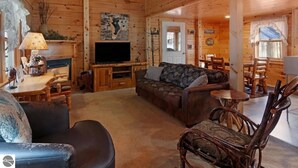 A cozy log cabin interior with a sofa, chairs, a television, and a fireplace. - Private Wooded Log Cabin Near Shanty Creek Resorts -Four Season Adventure Awaits (Bellaire)