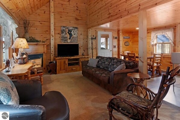 Interior acogedor de una cabaña de madera con sofá, sillones, televisor y chimenea.
