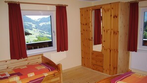 Une chambre à coucher avec deux lits en bois, une armoire et une fenêtre donnant sur un paysage montagneux.