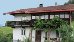 Une maison à deux étages avec un toit rouge, un balcon doté de balustrades en bois et une porte d’entrée.