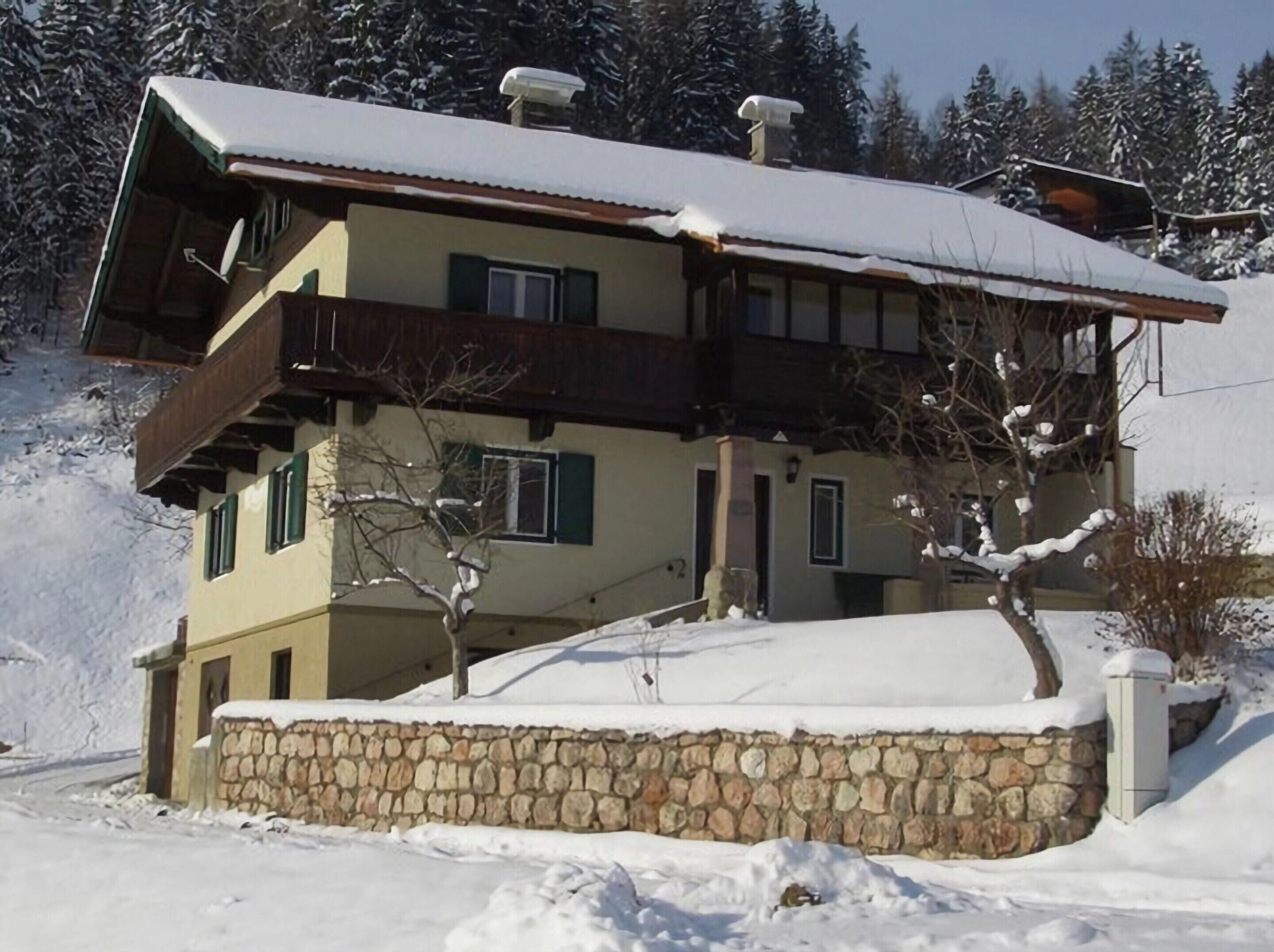 A two-story chalet with a stone foundation, wooden balconies, and a snow-covered roof.
