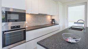 A modern kitchen with stainless steel appliances, a grey tiled backsplash, and a black granite countertop. - Corner Apartment in the Center With 3 Bedrooms (Middelkerke)