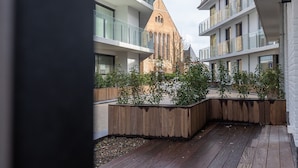 A courtyard with modern buildings, a wooden deck, and a historic tower. - Corner Apartment in the Center With 3 Bedrooms (Middelkerke)