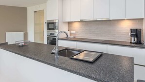 A modern kitchen with white cabinets, a stainless steel sink, and a built-in oven. - Corner Apartment in the Center With 3 Bedrooms (Middelkerke)