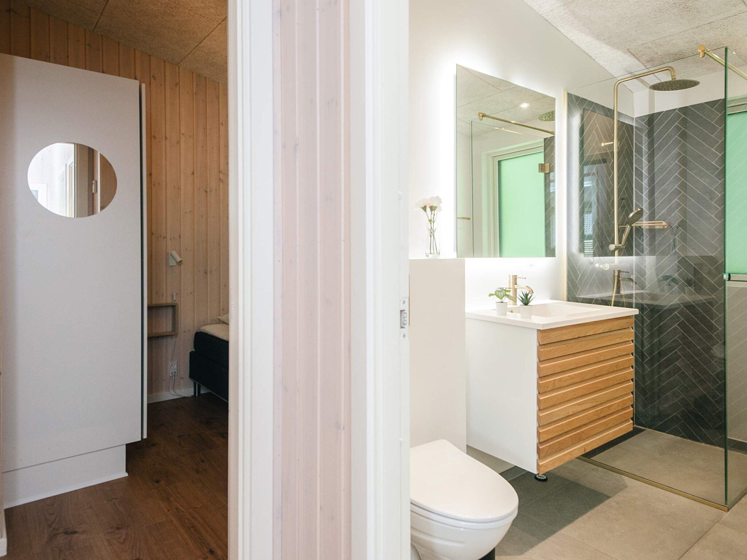 A modern bathroom with a wooden vanity, a white toilet, and a glass-enclosed shower area.