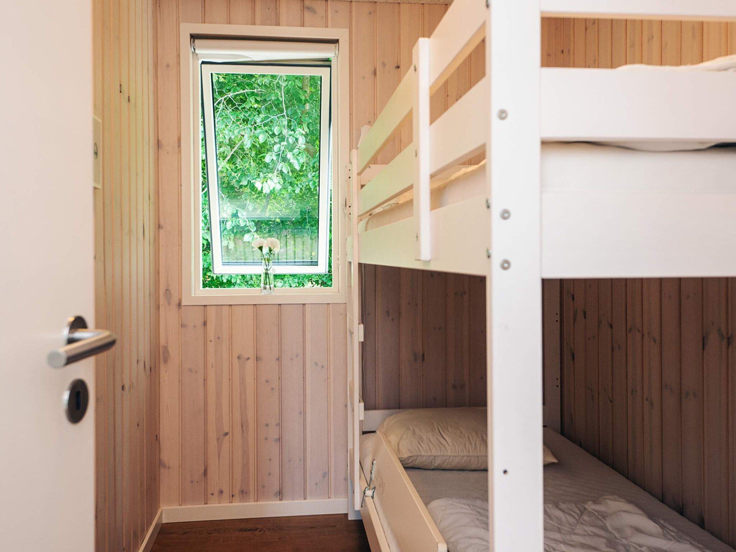 A bunk bed room with a window overlooking greenery.
