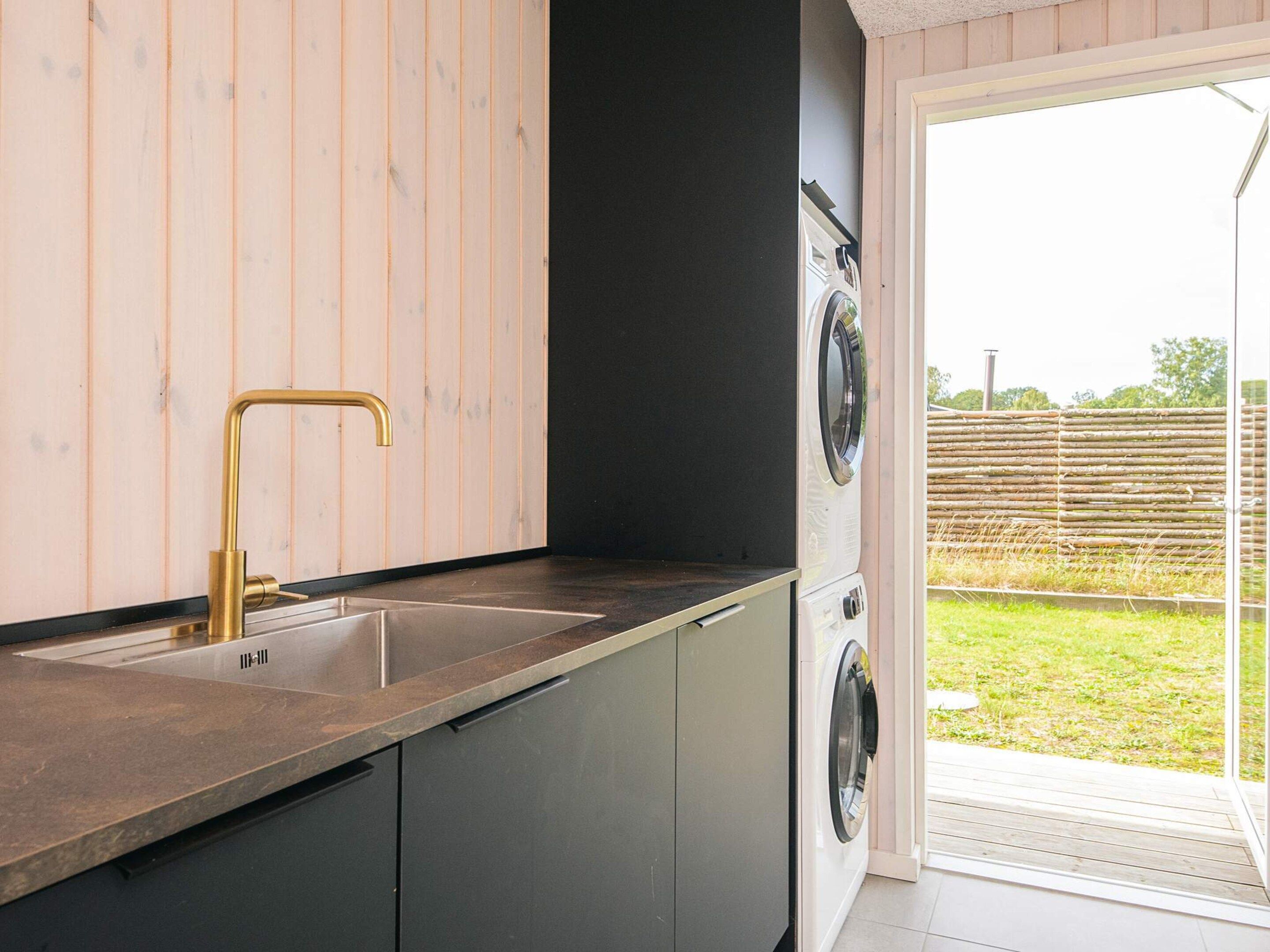 A kitchen with a sink, a washing machine, and a sliding glass door leading to an outdoor area.