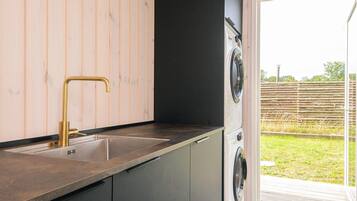 A kitchen with a sink, a washing machine, and a sliding glass door leading to an outdoor area.