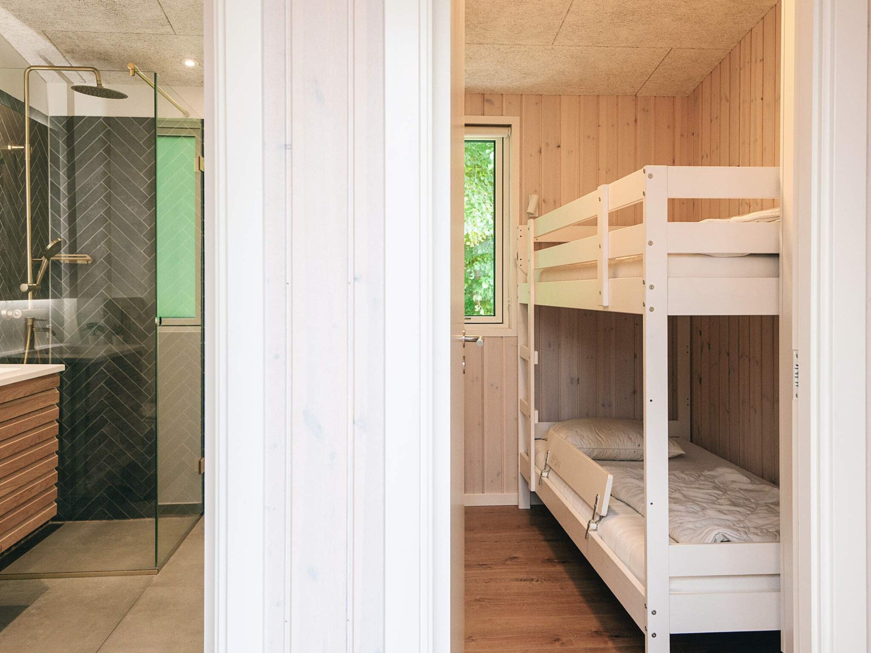 Ein kleines Zimmer mit Etagenbett, Glasdusche und einem Holznächtigungstisch.