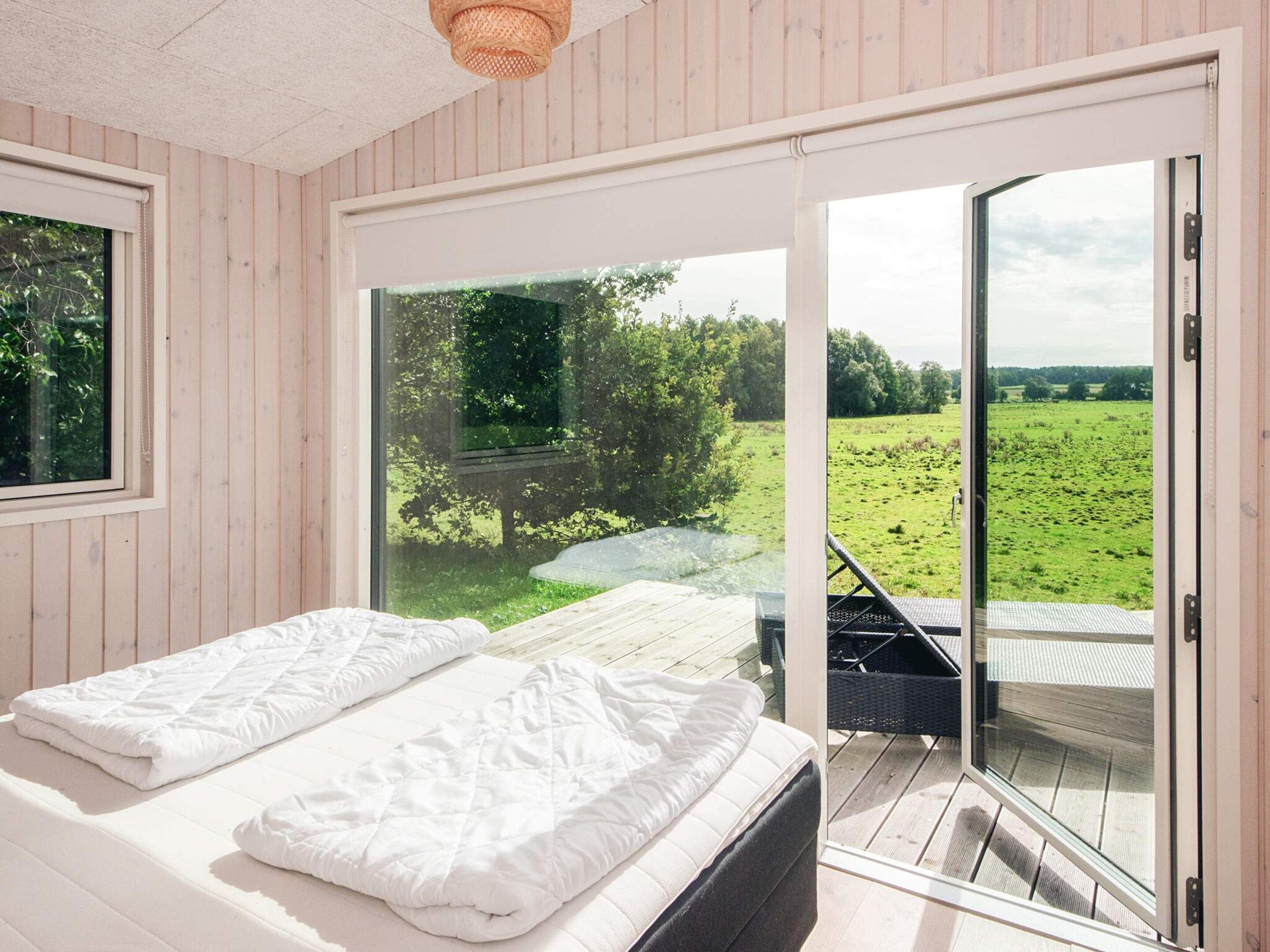 A bedroom with a bed, a window, and a view of a green field.