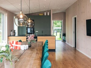 A modern kitchen with wooden cabinets, a central island, and a dining area with a long table and teal seating. - 14 Person Holiday Home in Glesborg (Glesborg)