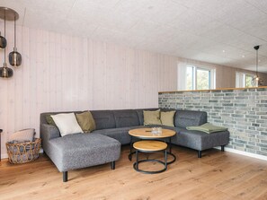 Una sala de estar moderna con un sofá modular, una mesa de centro redonda de madera y una pared de ladrillo decorativa.