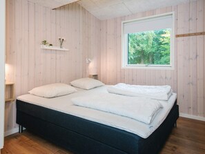 A bedroom with a bed, a window with a view of trees, and a shelf with decorative items. - 14 Person Holiday Home in Glesborg (Glesborg)