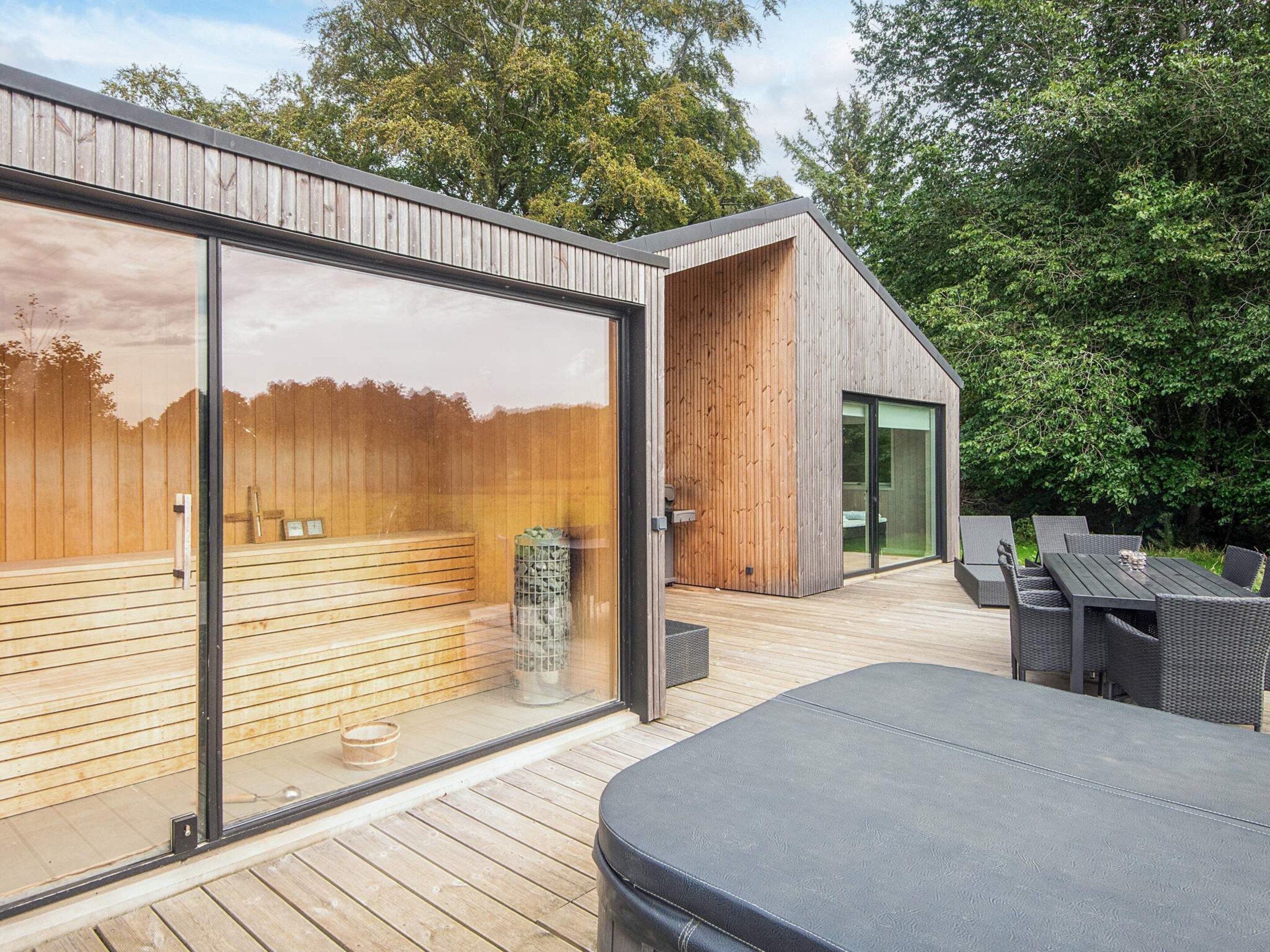 A modern outdoor deck with a wooden floor, a glass-enclosed sauna, and outdoor furniture.