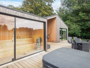 Eine moderne Außenterrasse mit Holzboden, einer gläsernen Sauna und Gartenmöbeln.