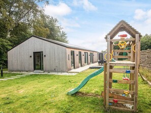 A modern building with a wooden exterior, a slide, and a climbing structure in a grassy area. - 14 Person Holiday Home in Glesborg (Glesborg)