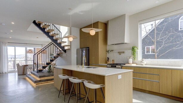 Une cuisine moderne dotée d’un îlot central, de tabourets de bar, d’un escalier et d’une grande fenêtre.