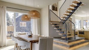 Une cuisine moderne avec un escalier en bois, un coin repas doté d’une grande table et de chaises, et une vue sur l’extérieur.