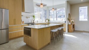 Une cuisine moderne avec des meubles en bois, des appareils électroménagers en acier inoxydable, un grand îlot central doté de tabourets de bar et de grandes fenêtres offrant une vue sur la ville.