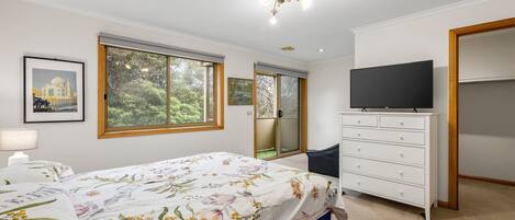 A bedroom with a bed, a dresser, a television, and a window with a view of greenery.