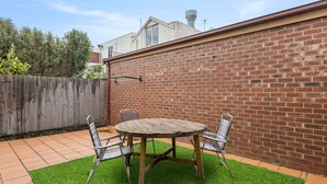A backyard with a brick wall, a wooden table, and two chairs. - Simpson Getaway 1 - Point Lonsdale (Point Lonsdale)