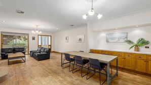 A spacious kitchen with a dining area, wooden cabinets, and a large window offering a view of the outdoors. - Simpson Getaway 1 - Point Lonsdale (Point Lonsdale)