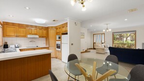 A modern kitchen with wooden cabinets, a central island, and a glass dining table with chairs. - Simpson Getaway 2 - Point Lonsdale (Point Lonsdale)