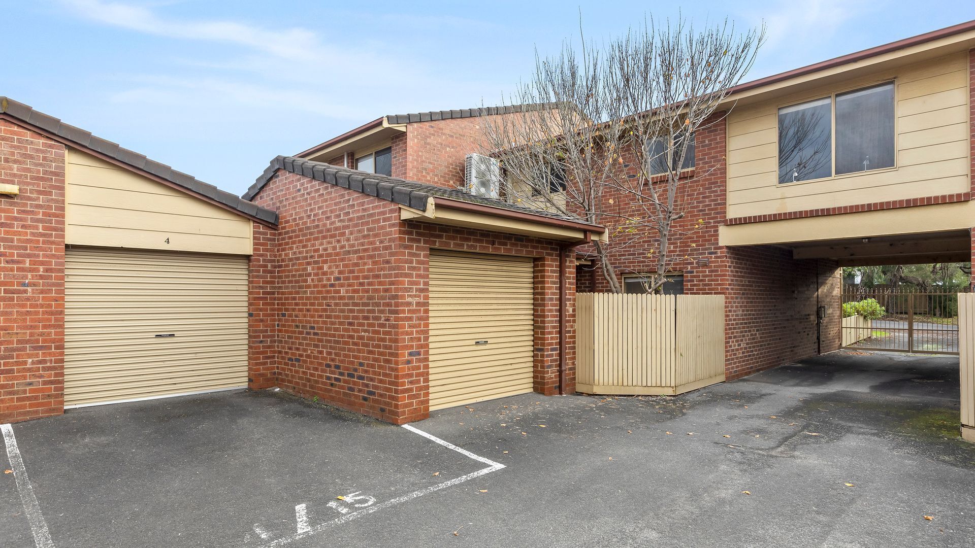 A two-story building with a brick facade, beige garage doors, and a fenced parking area.