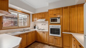 Cozinha com armários de madeira, micro-ondas, forno, pia e janela com vista para uma parede de tijolos.