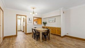 Uma sala de jantar com mesa e cadeiras de madeira, uma cozinha com armários de madeira e um corredor que dá para outro quarto.