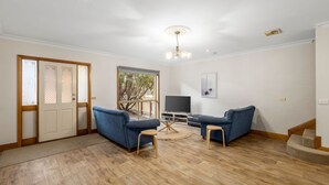 Uma sala de estar com dois sofás azuis, uma mesa de centro de madeira, uma TV em um móvel e uma janela grande com vista para árvores.