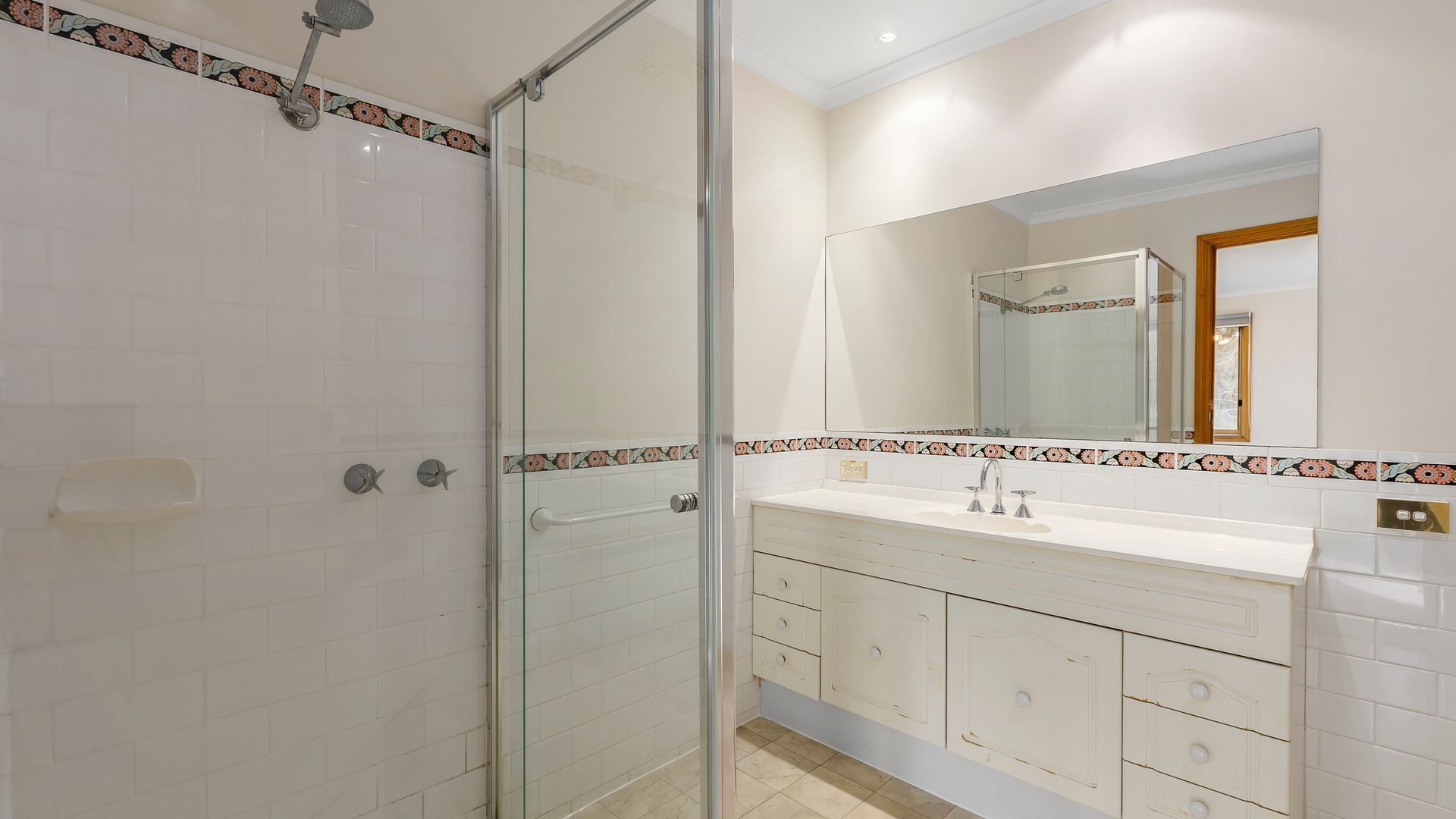 Een badkamer met een douchecabine van glas, een witte wastafel met een spiegel erboven en een betegelde spatwand.