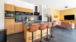 Une cuisine moderne dotée d’un îlot central, de meubles en bois et d’un four encastré. On trouve trois tabourets de bar devant l’îlot.