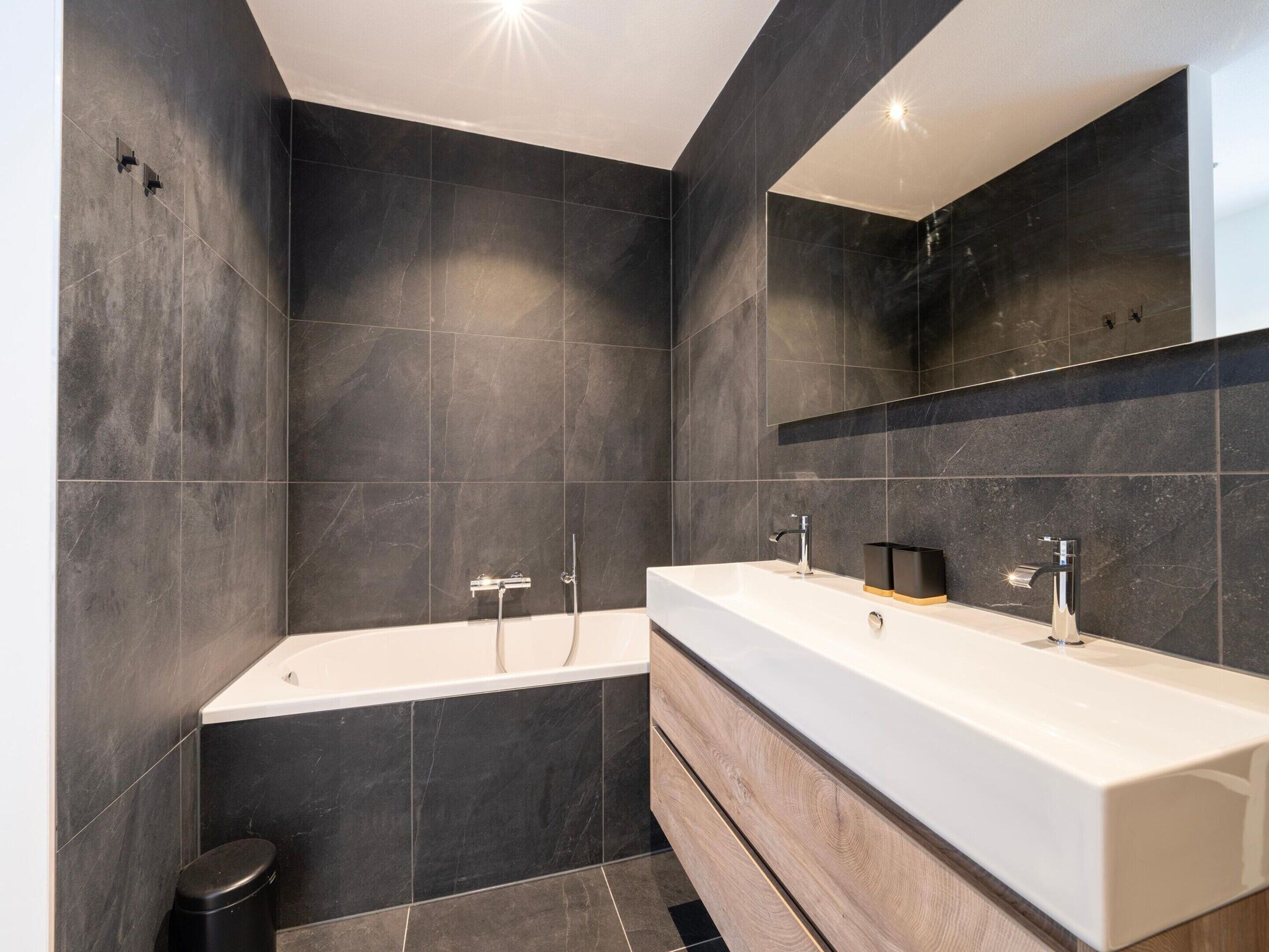 A modern bathroom with dark tiles, a white vanity, and a large mirror.